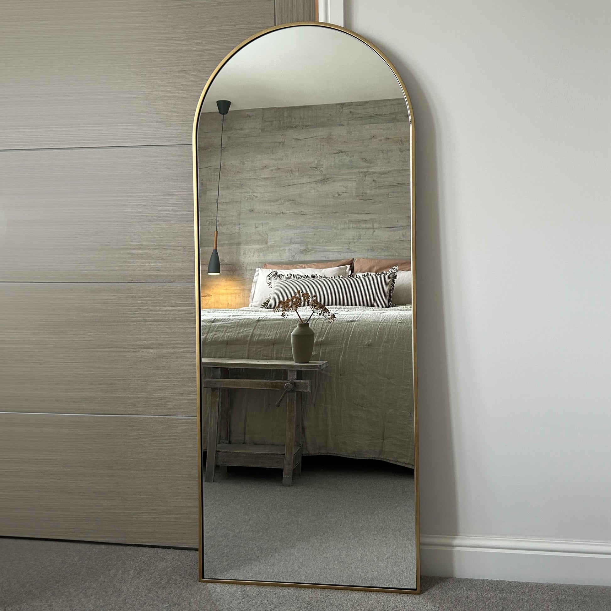 Full Length Dourado Large Arched Metal Mirror leaning against wall in bedroom
